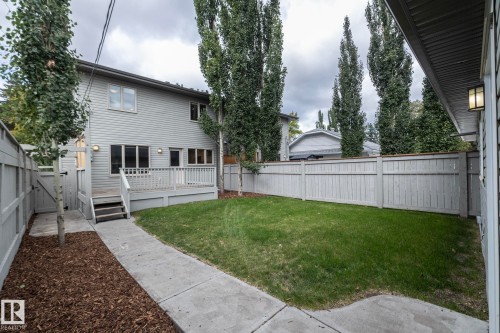Expansive backyard featuring a manicured lawn, a private wood-plank fence, a raised wood deck with railing, and mature trees - 55 Michigan Street, Devon, AB 