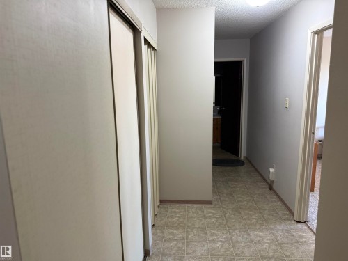 Hallway featuring light-toned walls, textured ceiling, tiled flooring, and multiple sliding closet doors - #414 3611 145 Av Nw, Edmonton, AB 