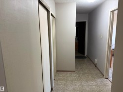 Hallway featuring light-toned walls, textured ceiling, tiled flooring, and multiple sliding closet doors - 