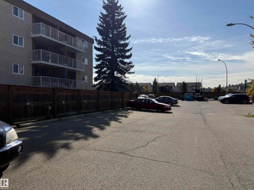Multi-story building featuring balconies with white railings, a robust wood fence, and paved parking - #414 3611 145 Av Nw, Edmonton, AB 