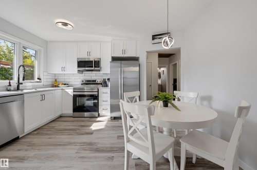 Kitchen with white cabinetry, stainless steel appliances, white subway tile backsplash, light wood-finish flooring, and a round dining table - 13655 122 Avenue Nw, Edmonton, AB 