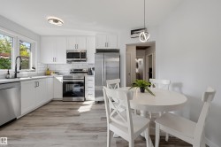 Kitchen with white cabinetry, stainless steel appliances, white subway tile backsplash, light wood-finish flooring, and a round dining table - 