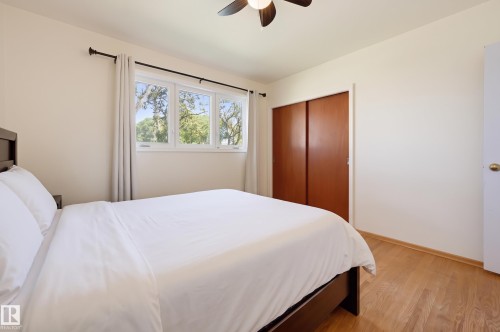 Hardwood-finish flooring, white walls, triple window, sliding wood-finish closet doors, and a ceiling fan - 13655 122 Avenue Nw, Edmonton, AB 