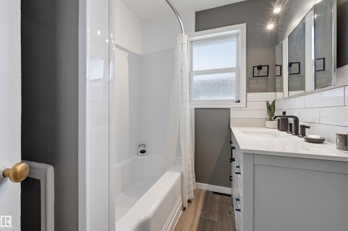 White subway tile backsplash, white vanity with black hardware, matte black faucet, integrated sink, and wood-finish flooring - 13655 122 Avenue Nw, Edmonton, AB 