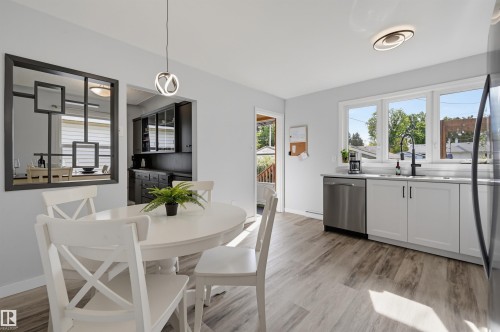 White shaker-style cabinetry with matte black hardware, stainless steel appliances, wood-finish flooring, and a large window above the sink - 13655 122 Avenue Nw, Edmonton, AB 