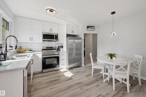 White cabinetry with dark hardware, stainless steel appliances, light-toned wood-finish flooring, white subway tile backsplash, and light countertops - 13655 122 Avenue Nw, Edmonton, AB 