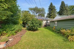 Expansive green lawn with established shrubbery, mature trees, and a detached structure with siding - 