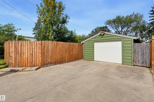 Detached garage with green siding and a white garage door, featuring a concrete driveway and a wood privacy fence - 13655 122 Avenue Nw, Edmonton, AB 