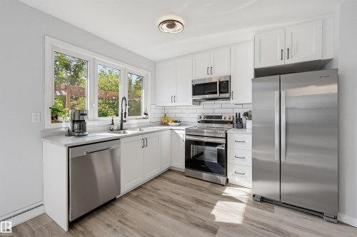 White cabinetry, stainless steel appliances, wood-finish flooring, subway tile backsplash, and a large window - 13655 122 Avenue Nw, Edmonton, AB 