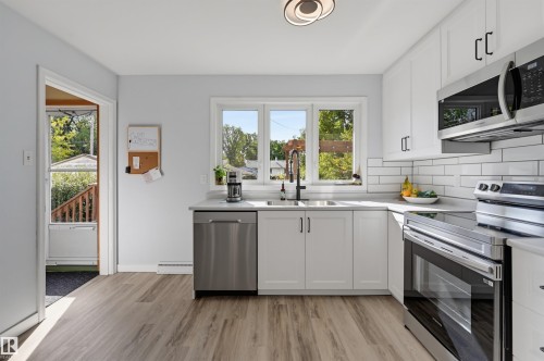 White cabinetry with matte black hardware, wood-finish flooring, stainless steel appliances, white subway tile backsplash, and a contemporary ceiling light fixture - 13655 122 Avenue Nw, Edmonton, AB 