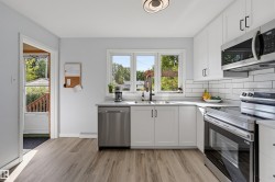 White cabinetry with matte black hardware, wood-finish flooring, stainless steel appliances, white subway tile backsplash, and a contemporary ceiling light fixture - 
