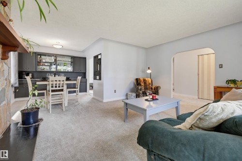 Light-toned carpeting throughout, stone accent wall, recessed lighting, arched doorway, and built-in cabinetry with glass-front uppers - 13655 122 Avenue Nw, Edmonton, AB 