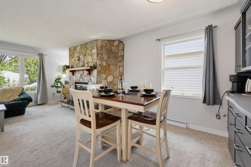 Stone-clad fireplace with wood mantle, large bay window, neutral carpeting, and built-in cabinetry - 13655 122 Avenue Nw, Edmonton, AB 