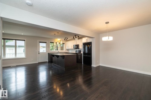 Expansive open-concept living space featuring dark wood-finish flooring, a contemporary kitchen island, white cabinetry, and recessed lighting - 53 Michigan Street, Devon, AB 