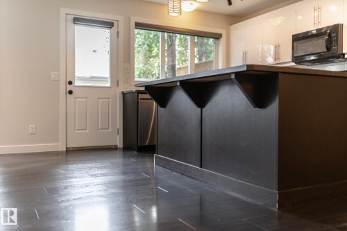 Dark wood-finish flooring, kitchen island with counter seating, high-gloss white cabinetry, and stainless steel dishwasher - 53 Michigan Street, Devon, AB 