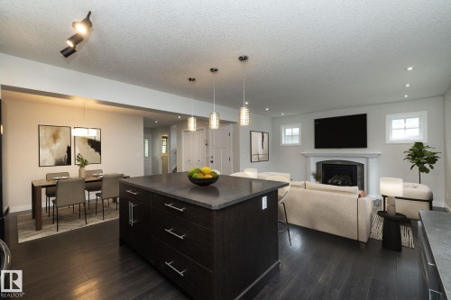 Dark wood-finish flooring throughout, featuring a kitchen island with stone countertop, a dining area with pendant lighting, and a living area with a fireplace and mantel - 53 Michigan Street, Devon, AB 