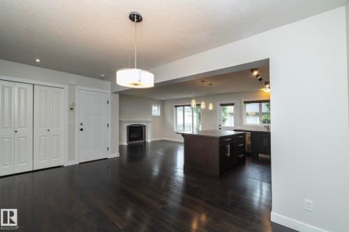 Dark wood-finish flooring, white bifold closet doors, fireplace with a white mantel, kitchen island with dark cabinetry, and pendant lighting fixtures - 53 Michigan Street, Devon, AB 