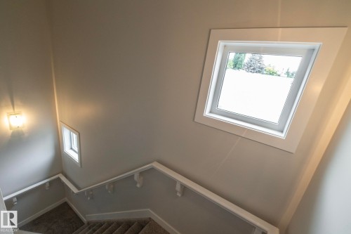 Angled window with white trim, wall-mounted sconce, and carpeted staircase with white railings - 53 Michigan Street, Devon, AB 