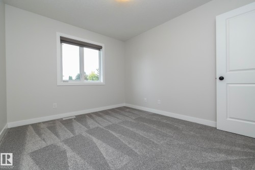 Neutral wall paint, patterned carpet flooring, white trim, white paneled door with black hardware, and a window with a roller shade - 53 Michigan Street, Devon, AB 