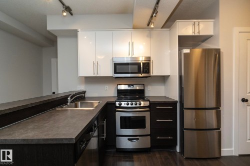 Kitchen featuring stainless steel appliances, track lighting, a double basin sink, and a two-toned cabinetry design - 53 Michigan Street, Devon, AB 