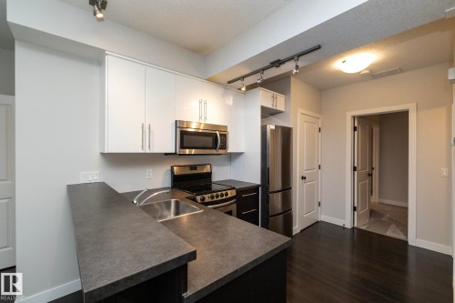 Kitchen featuring dark countertops, stainless steel appliances, white cabinetry, and wood-finish flooring - 53 Michigan Street, Devon, AB 