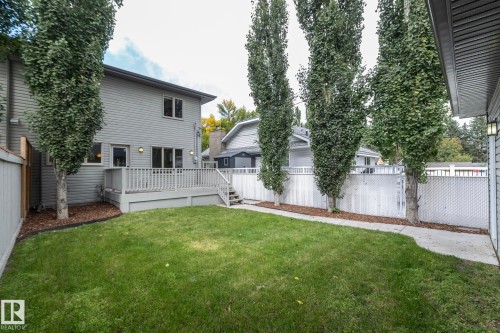 Expansive backyard with a manicured lawn, a large wooden deck with railing, and a concrete pathway - 53 Michigan Street, Devon, AB 