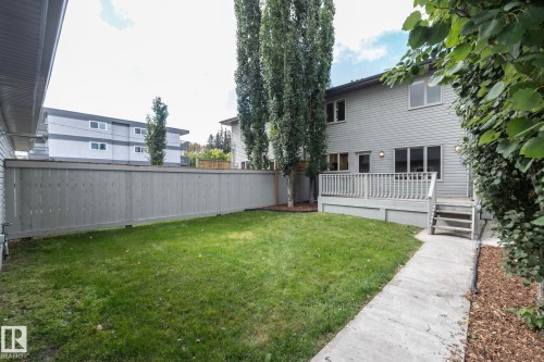 Expansive backyard featuring a manicured lawn, a gray wood fence, mature trees, a ground-level concrete pathway, and a gray wood deck with stairs - 53 Michigan Street, Devon, AB 