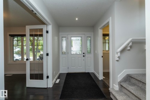 Entry foyer featuring a white multi-pane front door with sidelights, dark wood-finish flooring, and a carpeted staircase with white handrail - 53 Michigan Street, Devon, AB 