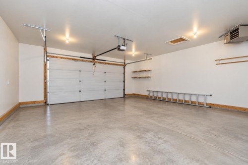 Attached garage with a white sectional door, exposed concrete flooring, and ceiling-mounted lighting - 53 Michigan Street, Devon, AB 