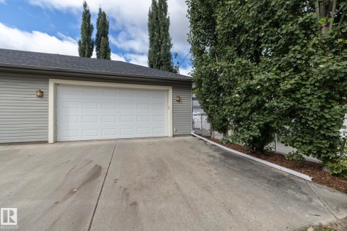 Attached garage with a white panel door, light gray siding, and a dark shingle roof - 53 Michigan Street, Devon, AB 