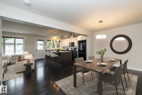 Open-concept living space featuring dark wood-finish flooring, a kitchen island with pendant lighting, and a dining area with a modern chandelier - 53 Michigan Street, Devon, AB 