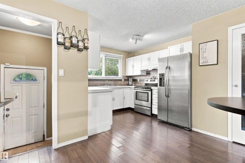 Kitchen featuring white cabinetry, stainless steel appliances, wood-finish flooring, and a tiled backsplash - 12 Hughes Road Nw, Edmonton, AB 