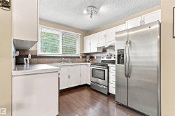 Kitchen featuring white cabinetry, stainless steel appliances, wood-finish flooring, and a window with blinds - 