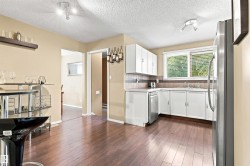 Kitchen featuring wood-finish flooring, white cabinetry, a stainless steel dishwasher, a stainless steel refrigerator, and a window with blinds - 