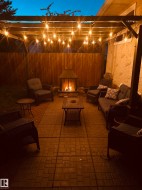 Expansive paver patio with a built-in outdoor fireplace and a wood pergola featuring string lighting - 