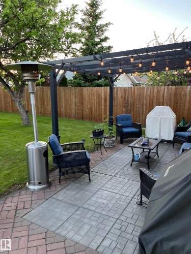 Expansive patio featuring a dark-toned pergola with integrated lighting, a privacy fence, and mature trees surrounding the property - 12 Hughes Road Nw, Edmonton, AB 