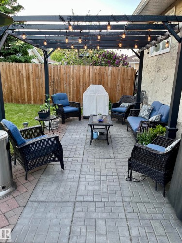 Paved patio area featuring a pergola with string lighting and wood fencing - 12 Hughes Road Nw, Edmonton, AB 