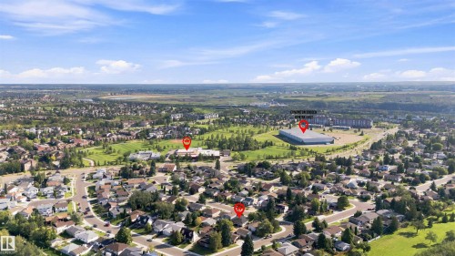 Aerial perspective showcasing a residential neighborhood with surrounding green spaces and distant commercial structures - 12 Hughes Road Nw, Edmonton, AB 