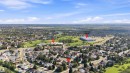 Aerial perspective showcasing a residential neighborhood with surrounding green spaces and distant commercial structures - 12 Hughes Road Nw, Edmonton, AB 