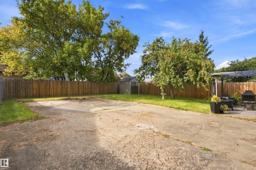 Expansive paved area with a perimeter wood fence, a separate storage shed, and mature trees - 12 Hughes Road Nw, Edmonton, AB 