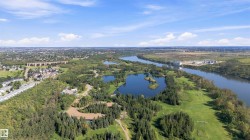 Expansive natural landscape featuring a prominent river, multiple serene lakes, dense mature trees, open grassy areas, and distant urban development - 