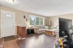 Entry door with decorative glass insert, wood-finish flooring, and a large window with blinds - 