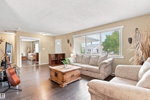 Expansive living area with wood-finish flooring, large windows, and neutral wall tones - 12 Hughes Road Nw, Edmonton, AB 