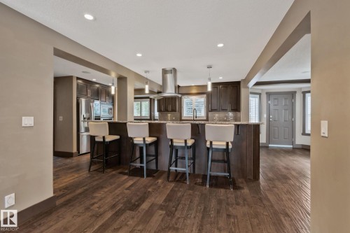 Kitchen featuring a large island with countertop seating, dark wood cabinetry, stainless steel appliances, and wood-finish flooring - 10 Eldorado Drive, St. Albert, AB 