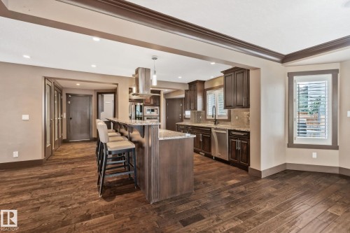 Wood-finish flooring throughout, kitchen island with built-in seating, dark wood cabinetry, stainless steel appliances, and a tiled backsplash - 10 Eldorado Drive, St. Albert, AB 