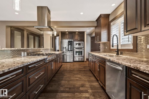 Expansive kitchen featuring wood-finish flooring, dark wood cabinetry, stainless steel appliances, and a mosaic tile backsplash - 10 Eldorado Drive, St. Albert, AB 