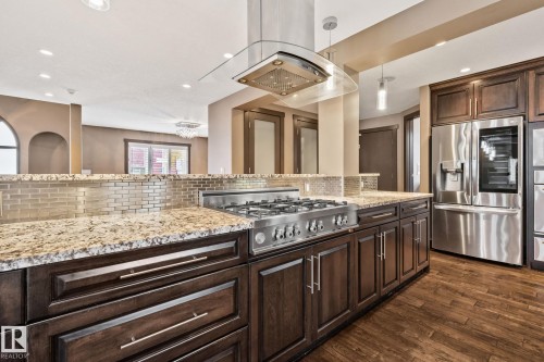 Gourmet kitchen with stainless steel appliances, a multi-burner gas range, custom wood cabinetry, granite countertops, and a tile backsplash - 10 Eldorado Drive, St. Albert, AB 