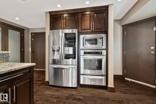 Stainless steel refrigerator and double oven, built-in microwave, dark wood-finish cabinetry, and wood-finish flooring - 10 Eldorado Drive, St. Albert, AB 