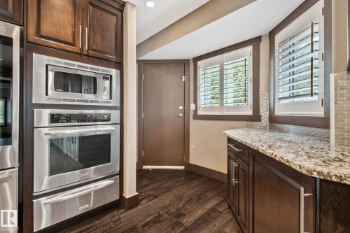 Built-in stainless steel double oven and microwave, dark wood-finish cabinetry, speckled countertop, and two windows with white louvered shutters - 10 Eldorado Drive, St. Albert, AB 