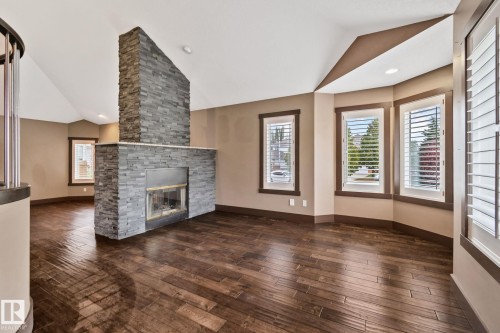 Stone-clad fireplace with a hearth, dark wood-finish flooring, and multiple windows with plantation shutters - 10 Eldorado Drive, St. Albert, AB 
